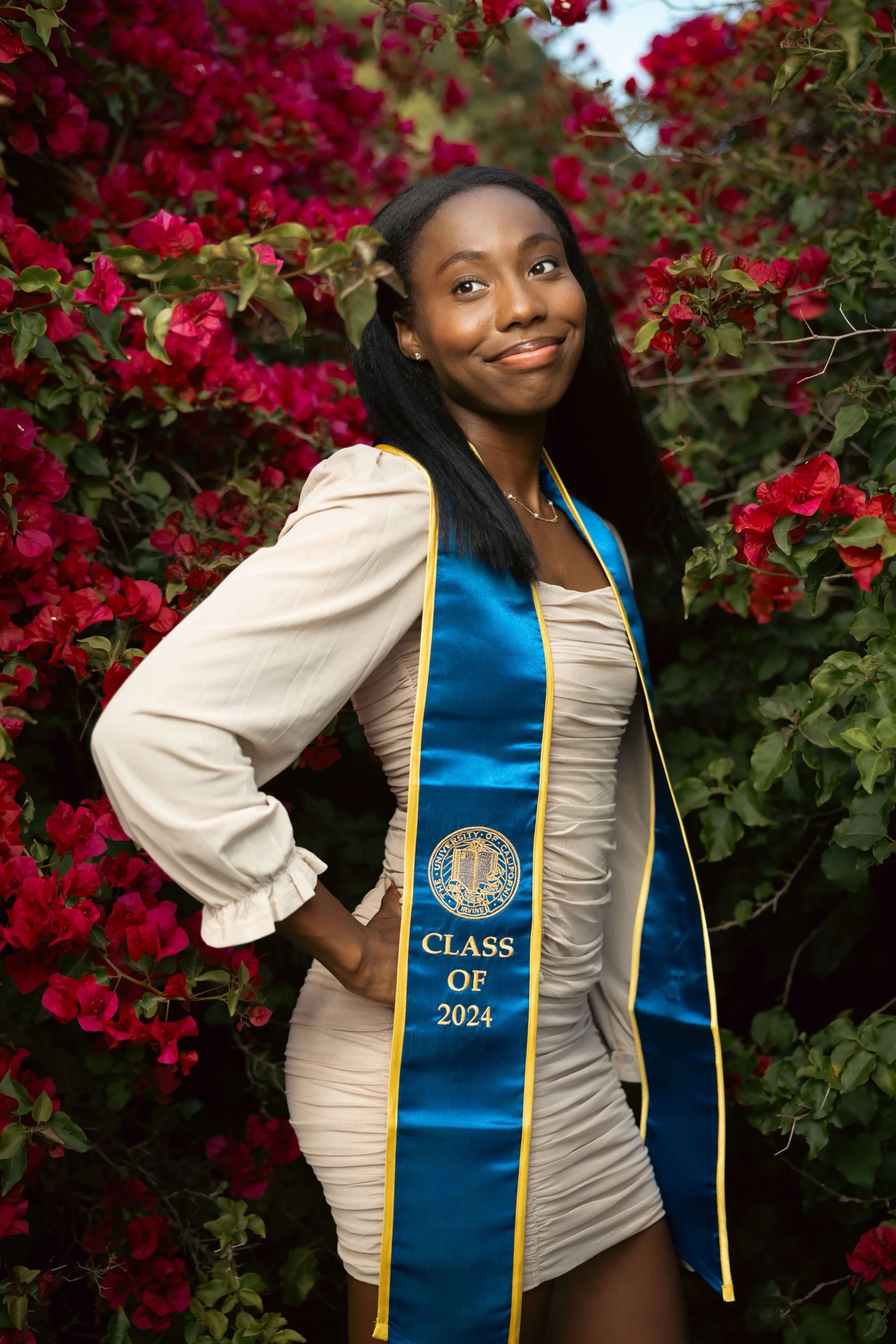 UCI graduate in cap and gown at red flower area