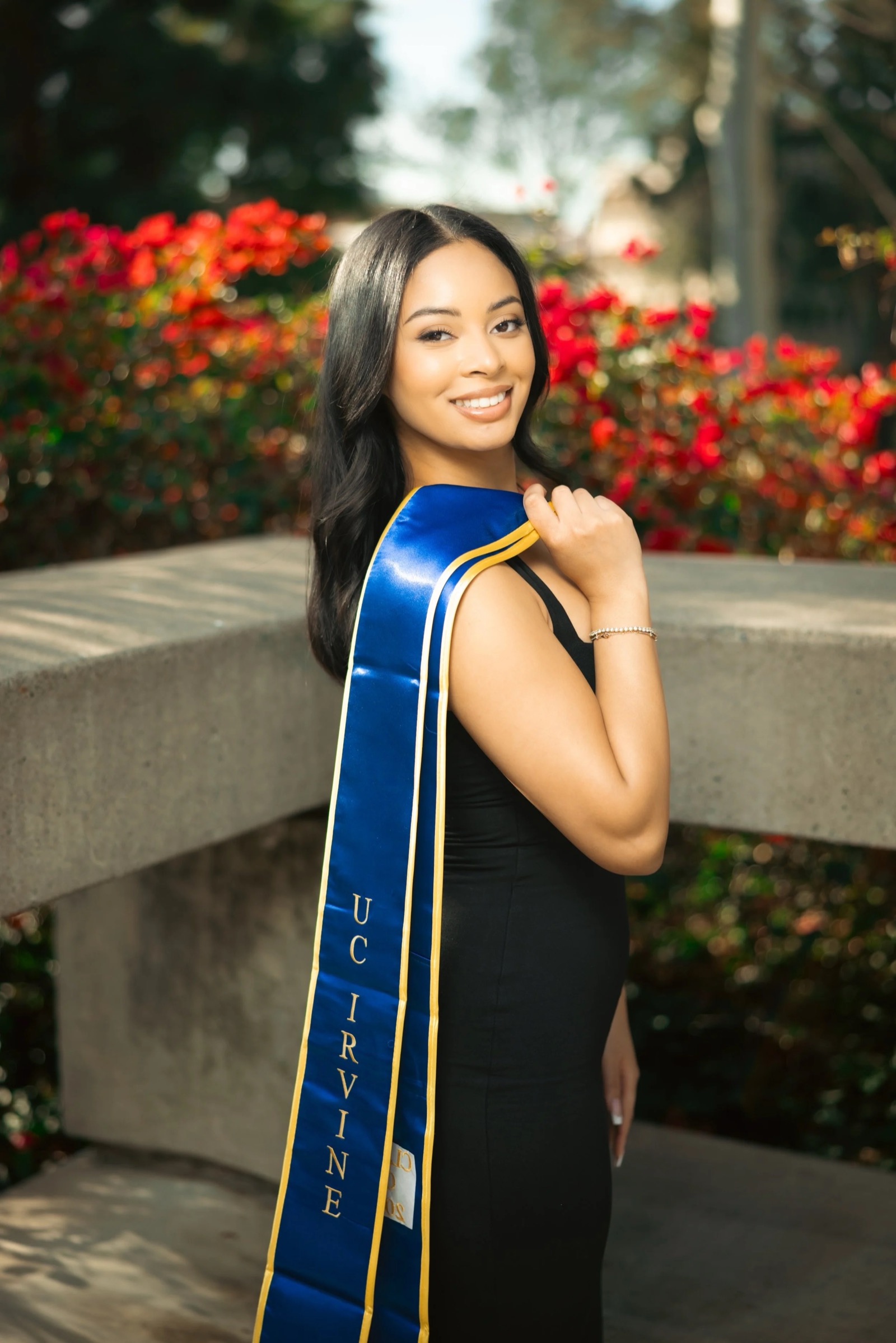 UCI graduate with sash at Aldrich Park red flowers