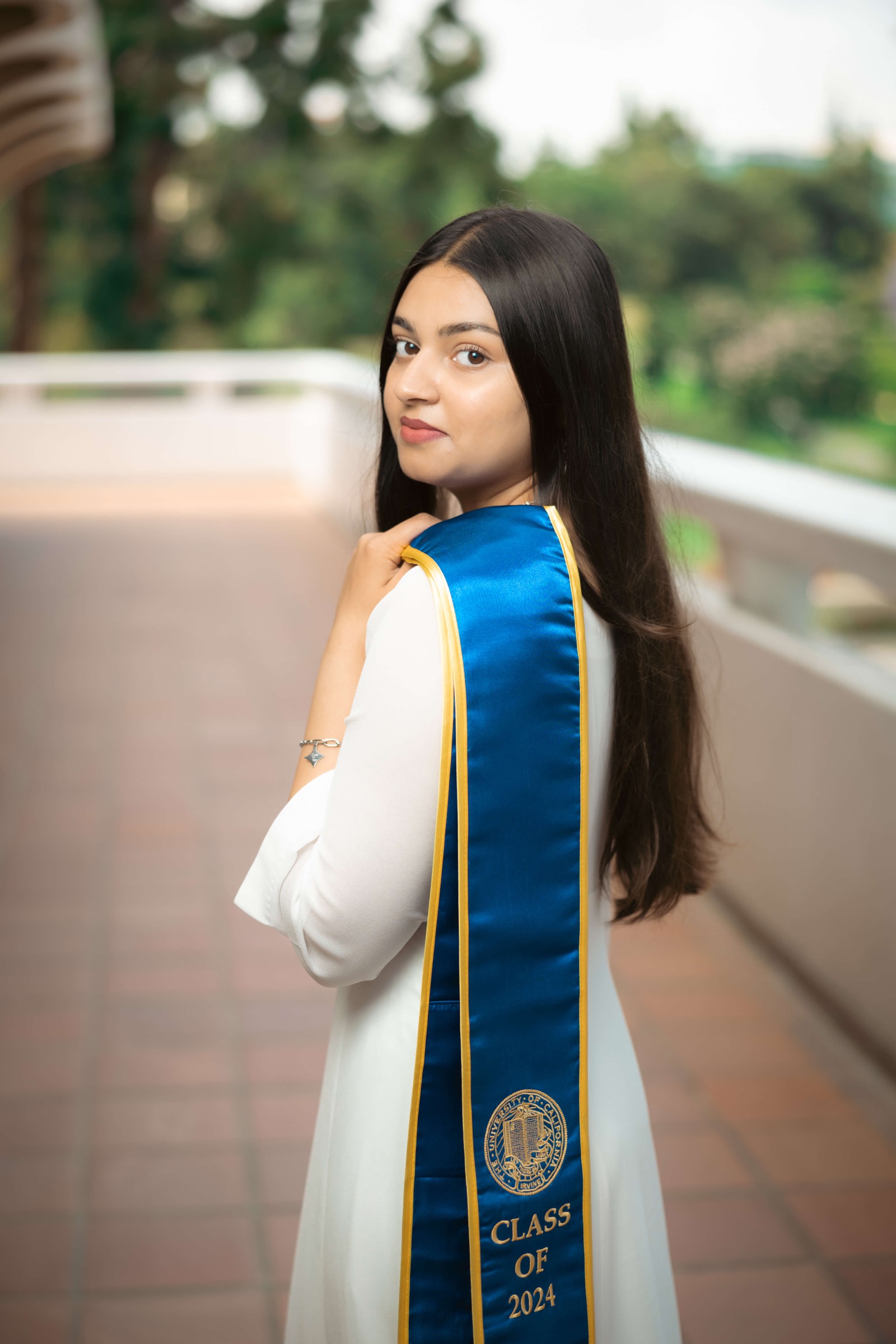 UCI graduate looking over shoulder with sash draped down her back