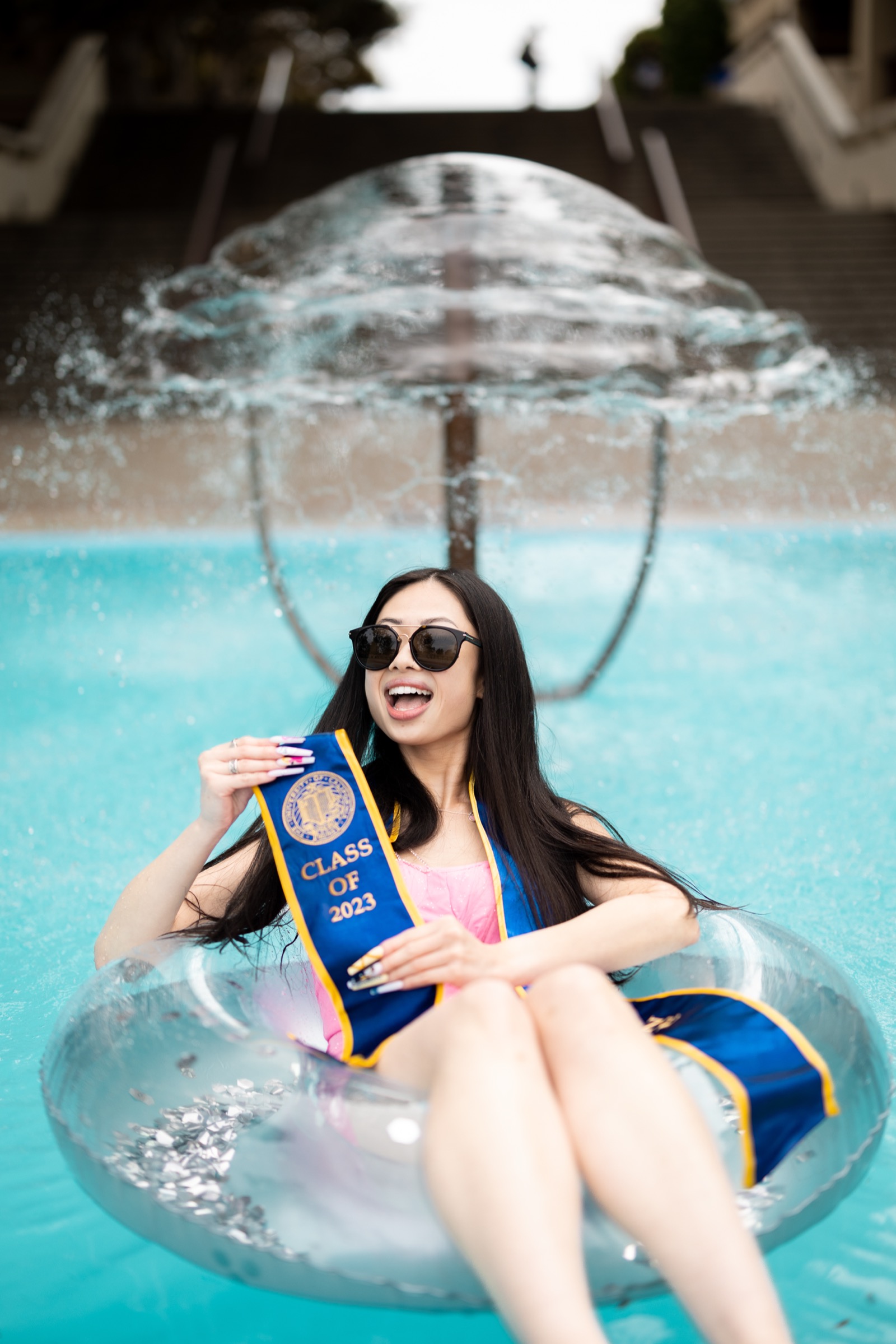 UCI graduate celebrating in pool with sash and sunglasses