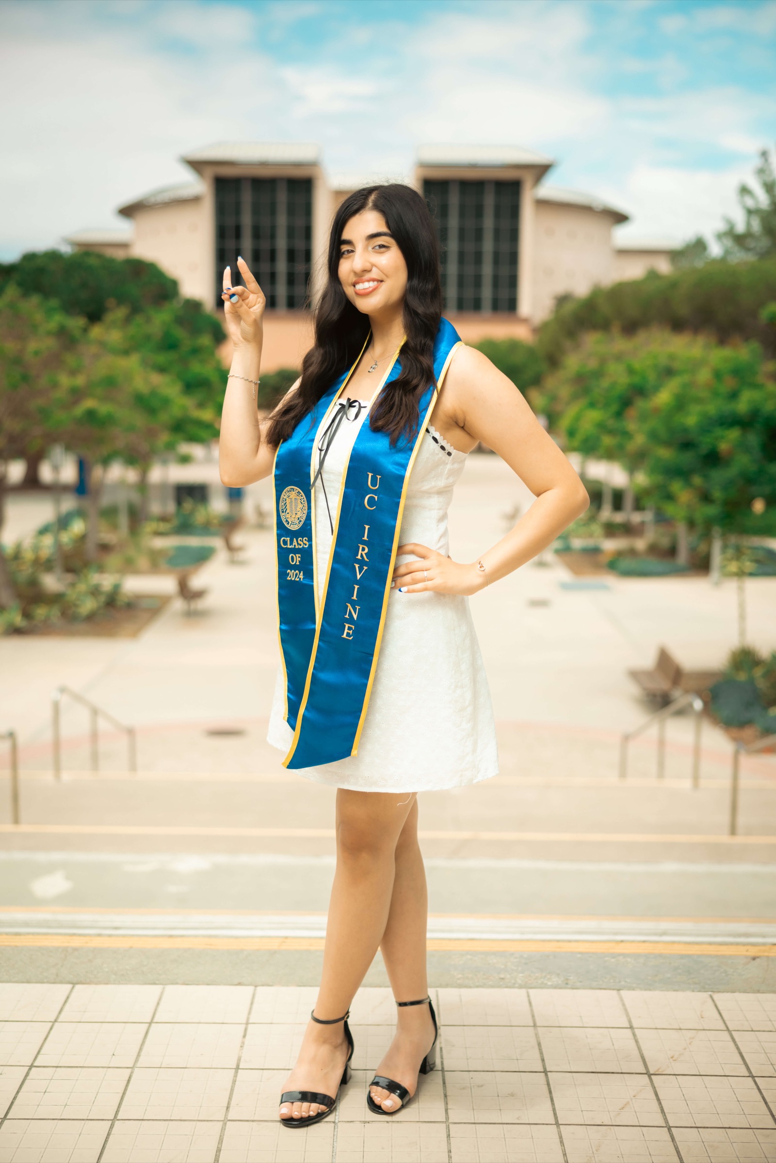 UCI graduate doing Zot Zot hand sign on campus with sash