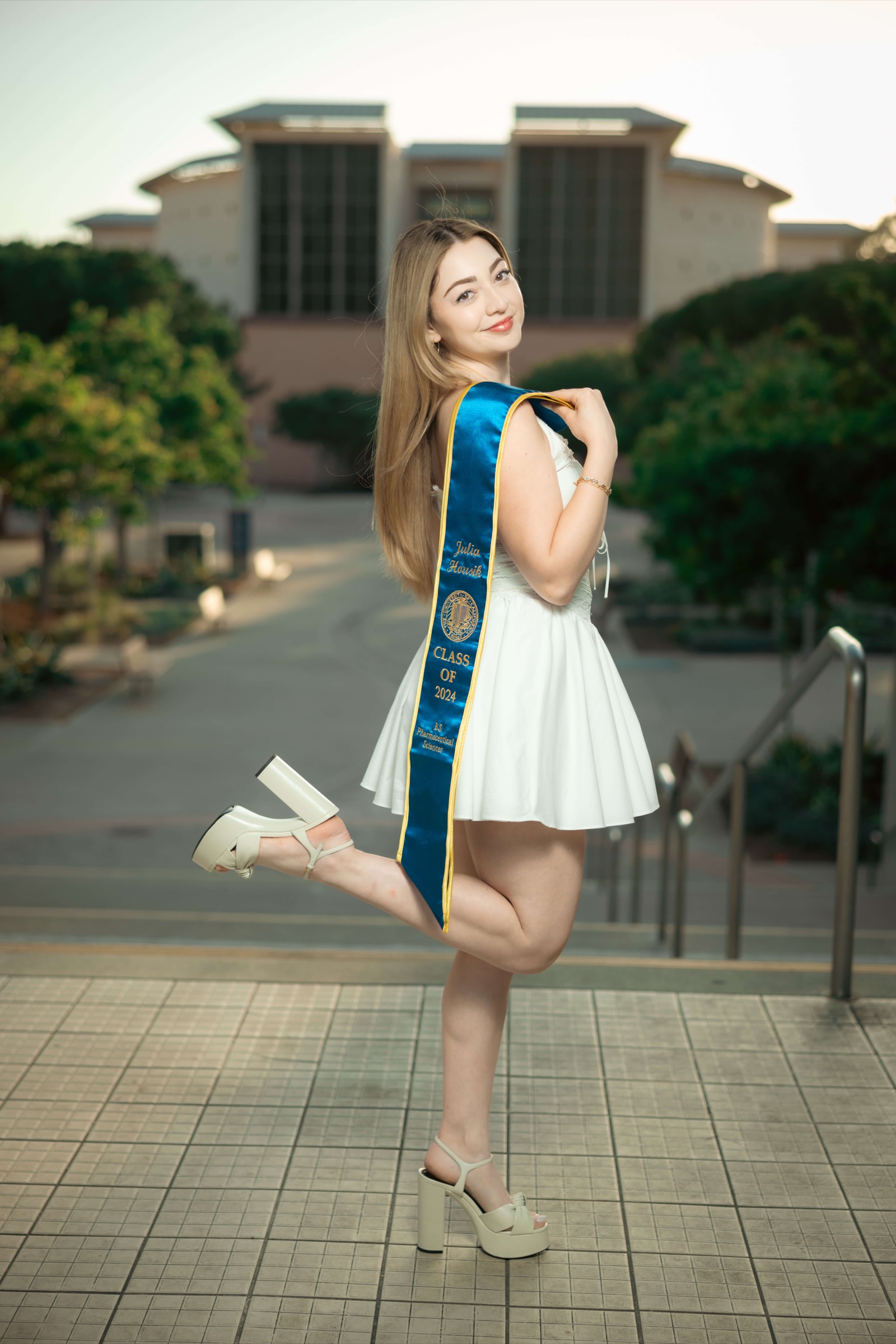 UCI graduate in white dress looking back over shoulder on campus steps